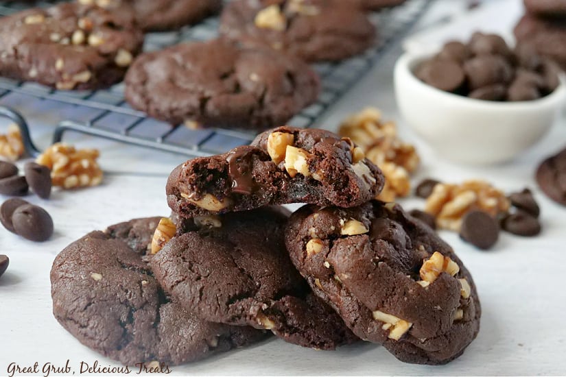 Dark chocolate cookies stacked on top of each other with walnuts, dark chocolate chips and additional cookies in the background.