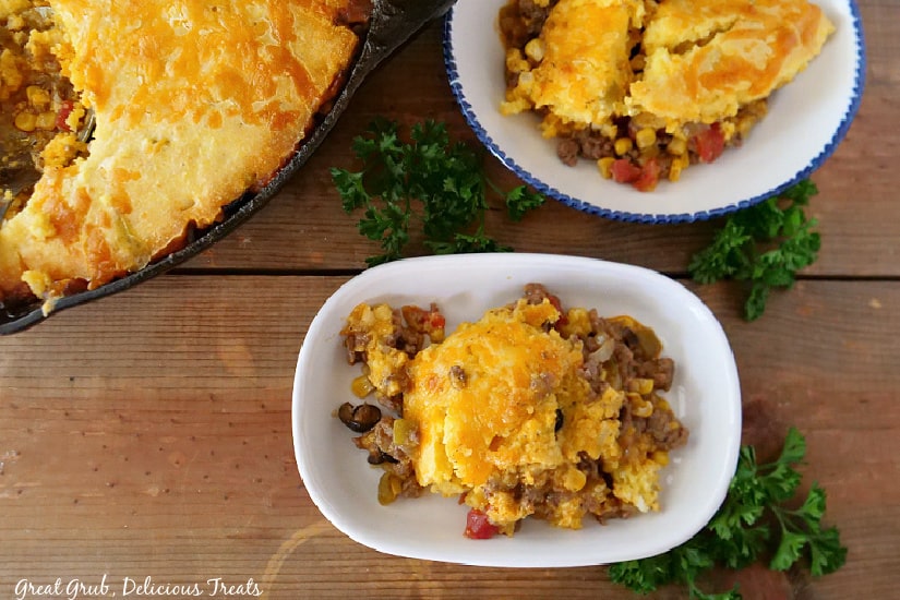 An overhead picture of Tamale Pie in a shallow white bowl with the cast iron pan full of Tamale Pie in the background.