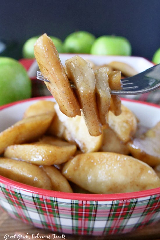 Four slices of fried apples on a fork, hovering over a bowl full of fried apples.