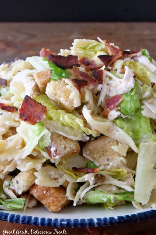 A close up photo of a white bowl filled with a Caesar pasta salad with chicken and bacon, and croutons.