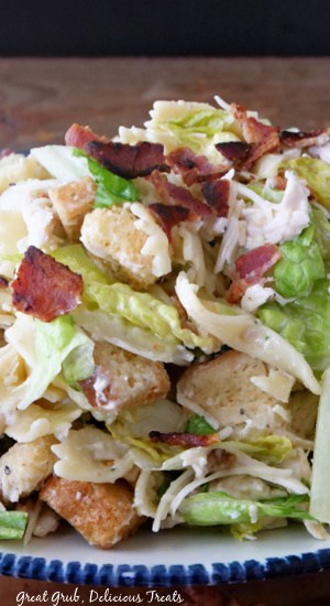 A close up photo of a Caesar salad with chicken, bacon, croutons.