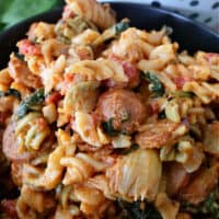 A black bowl filled with spinach, artichoke, chicken sausage and rotini pasta.