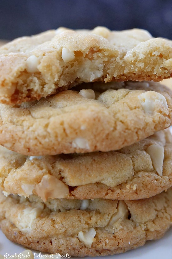 A close up photo of white chocolate macadamia nut cookies with a bite taken out of one so you can see the soft inside of the cookie.