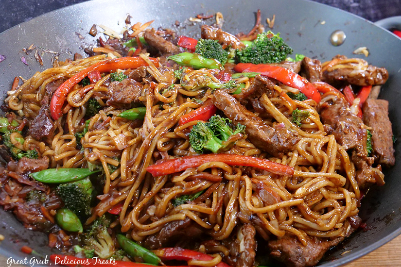 A large wok with lo mein noodles, veggies, and beef. 
