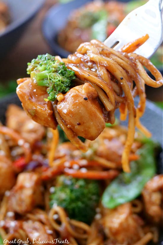 A bite of lo mein on a fork with chicken, broccoli, seasonings, and lo mein noodles.