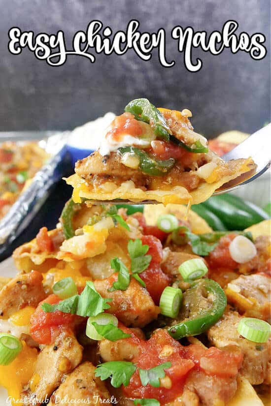 A serving of chicken nachos with a nacho on a fork and the title of the recipe at the top of the photo.