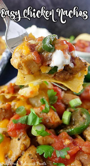 A close up of a fork holding a nacho with all the ingredients on it and the title of the recipe at the top of the photo.
