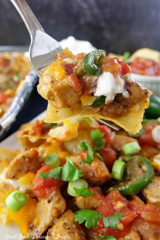 A close up of a fork holding a loaded chicken nacho.