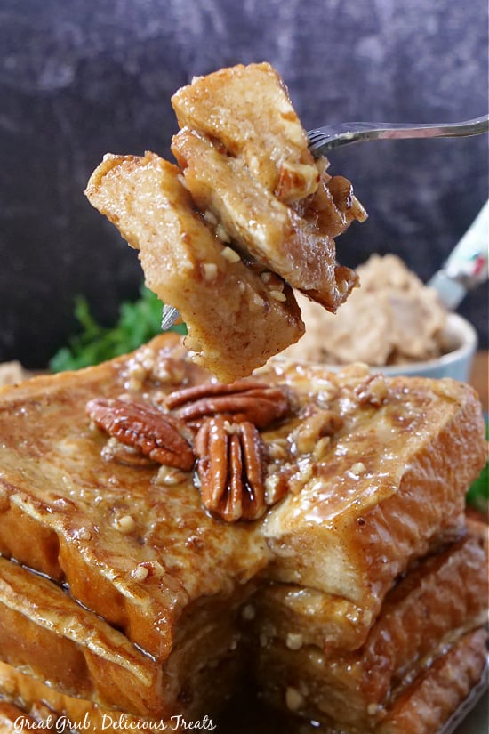 A bite of French toast on a fork, with a stack of French toast in the background.