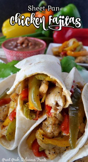 Three chicken fajitas stacked up on a white plate with a red bowl of charro beans in the background and all different colors of bell peppers.