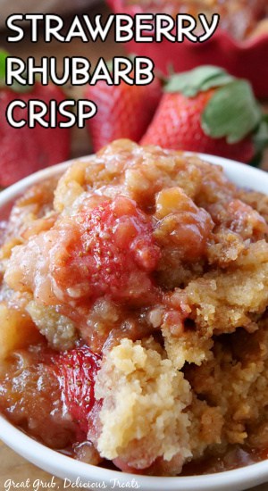 Strawberry rhubarb crisp in a white bowl with strawberries in the background for decoration.