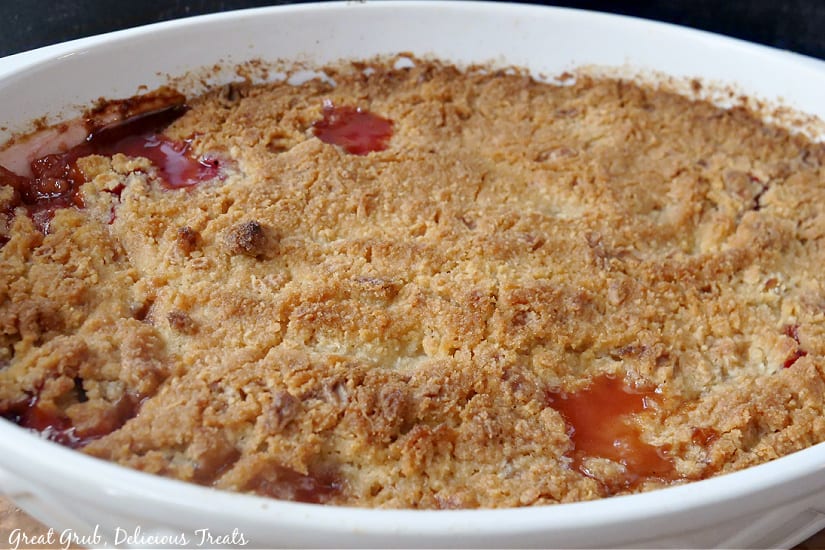 An oval white casserole dish filled with freshly baked strawberry rhubarb crisp.
