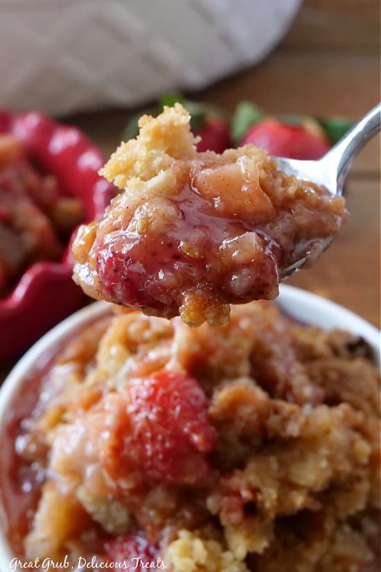 A bite of strawberry rhubarb crisp on a spoon with white bowl in the background.