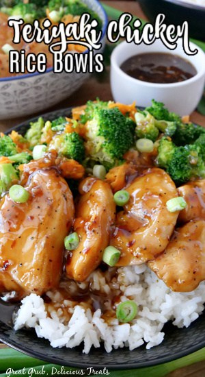 A black bowl filled with white rice, broccoli, carrots, chicken, and teriyaki sauce with a small white bowl filled with teriyaki sauce in the background.