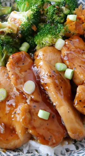 A close up picture of chicken, broccoli, carrots, and green onions over a bed of rice.