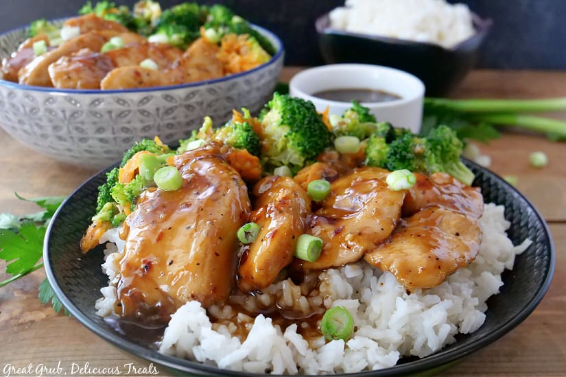 A black bowl filled with white rice, broccoli, carrots, chicken, green onions, and teriyaki sauce.