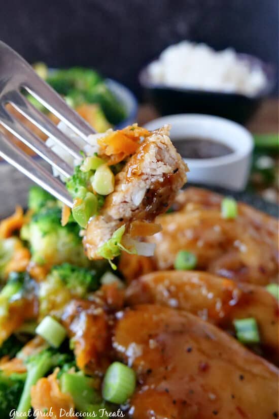 A close up picture of a bite of chicken with broccoli, carrots, and rice on a fork.