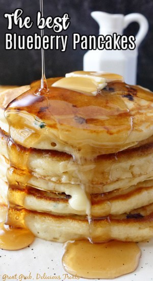 A stack of 5 blueberry pancakes, topped with butter, and drizzled with maple syrup.