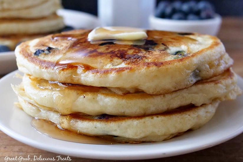 A stack of three blueberry pancakes topped with butter and syrup.