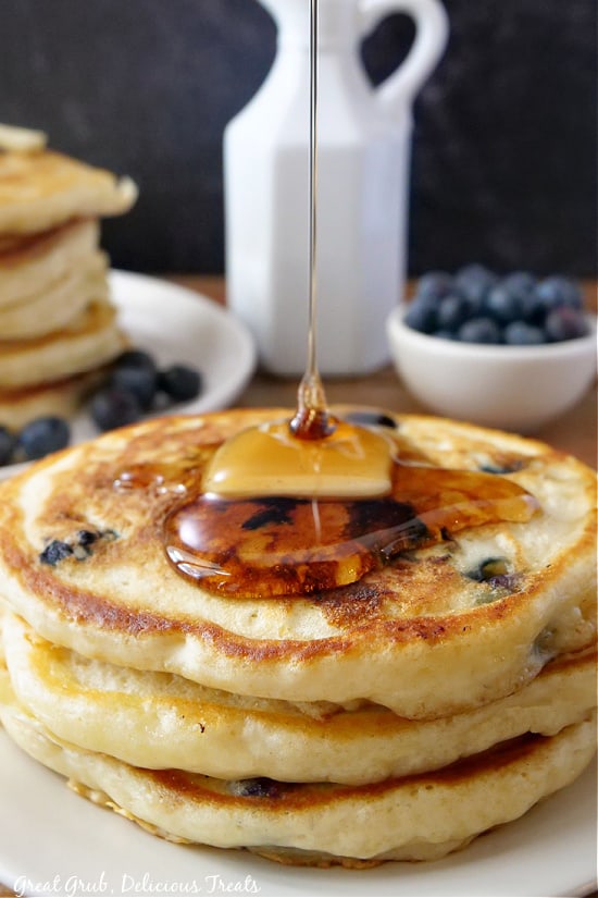A stack of three pancakes stacked on a white plate with maple syrup being drizzled on the top. 