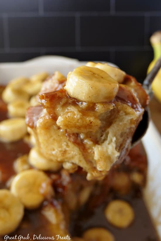 A bite of bread pudding covered in a glaze and a sliced banana on top.