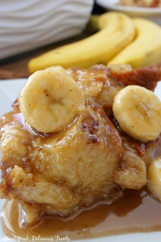 A serving of banana bread pudding on a white plate covered with a delicious glaze and sliced bananas.