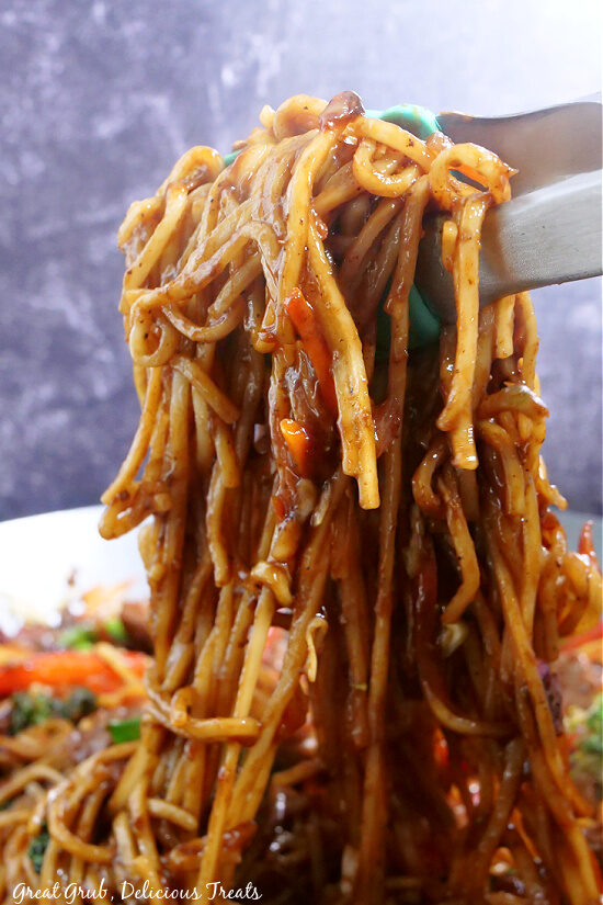 Noodles coated in a homemade sauce that is lifted up with tongs.