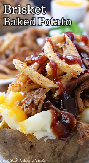 A close up photo of brisket baked potatoes with onion strings, cheese, and barbecue sauce.