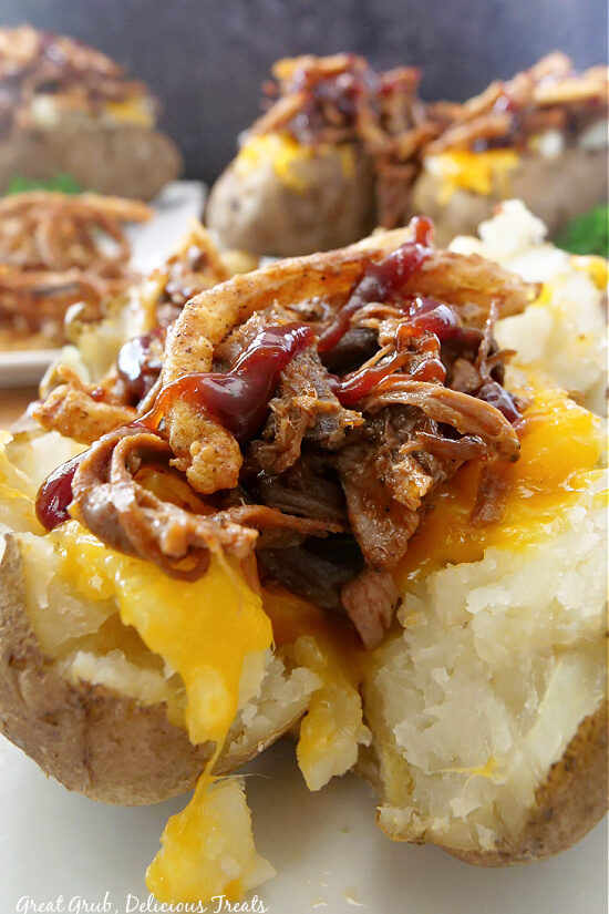 A baked potato cut in half, topped with cheese, brisket, onion strings, and drizzled with barbecue sauce.
