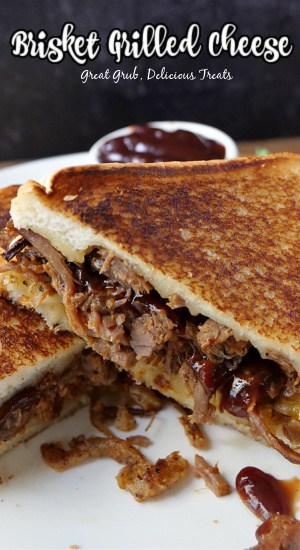 A close-up picture of a brisket grilled cheese cut in half with a small bowl of barbeque sauce in the background.