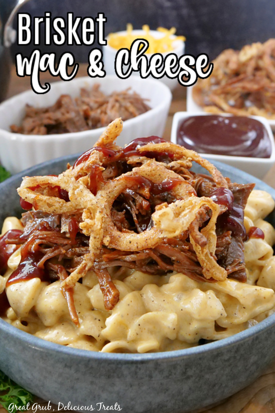 A gray bowl filled with mac and cheese, a small white bowl in the background filled with shredded brisket, and another bowl filled with BBQ sauce.