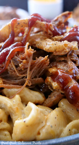 A close up pic of mac and cheese topped with BBQ sauce, brisket, and onion strings 