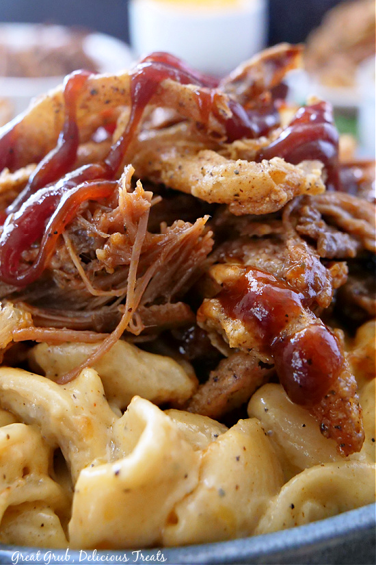 A close up pic of macaroni and cheese topped with brisket, BBQ sauce, and onion strings.