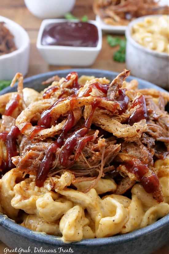 A bowl of mac and cheese and a small bowl of BBQ sauce, mac and cheese, and brisket in the background. 