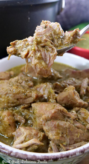 A large bite of pork chili verde with a bowl full in the background.