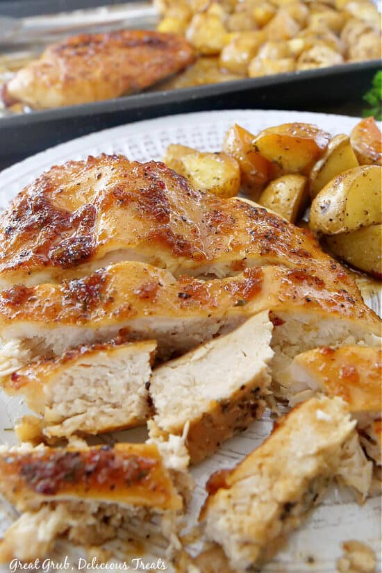A close-up picture of sheet pan chicken and potatoes on a white plate with pieces of the chicken cut up.