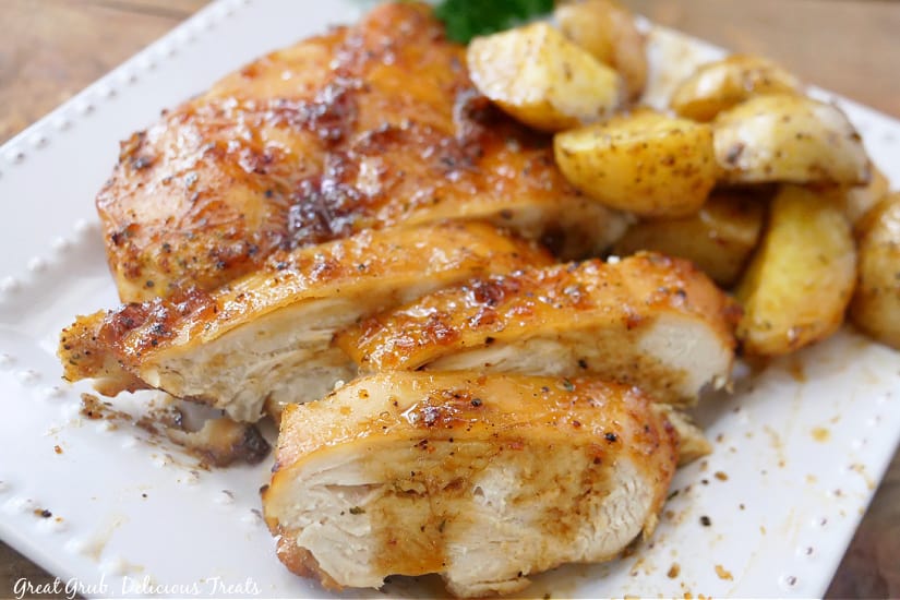 A horizontal picture of sheet pan chicken and potatoes on a white plate with parsley in the background.