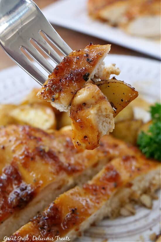 Sheet pan chicken and potatoes on a fork with a plate of chicken and potatoes in the background.