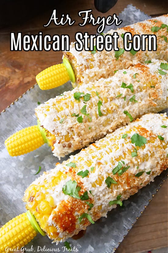 Three ears of corn that have been covered with a mixture that is popular with street corn on a silver tray.