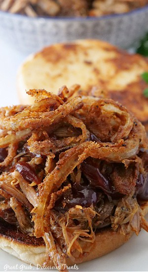 A close-up picture of a BBQ pulled pork sandwich that is topped with barbecue sauce and fried onion strings.