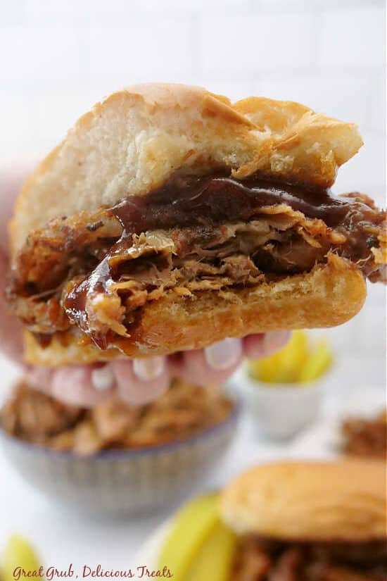 Half of a pulled pork sandwich with a bite taken out of it being held close to the camera lens.