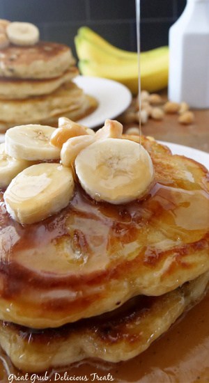 Maple syrup being drizzled on banana nut pancakes, with a plate of pancakes in the back for deocration.