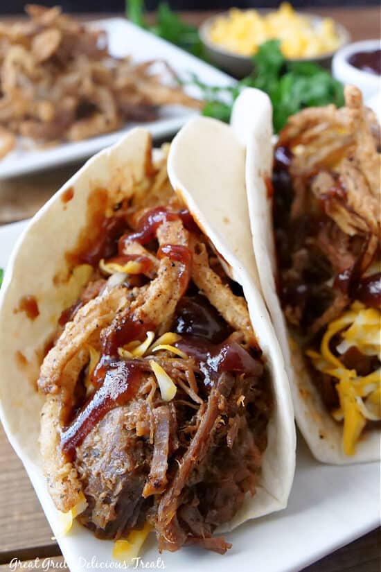 A white plate with tacos on it that are made with leftover beef brisket.