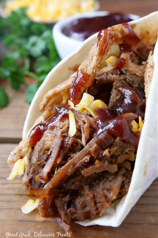 A close up of leftover brisket in a flour tortilla with cheese, onion strings and BBQ sauce.