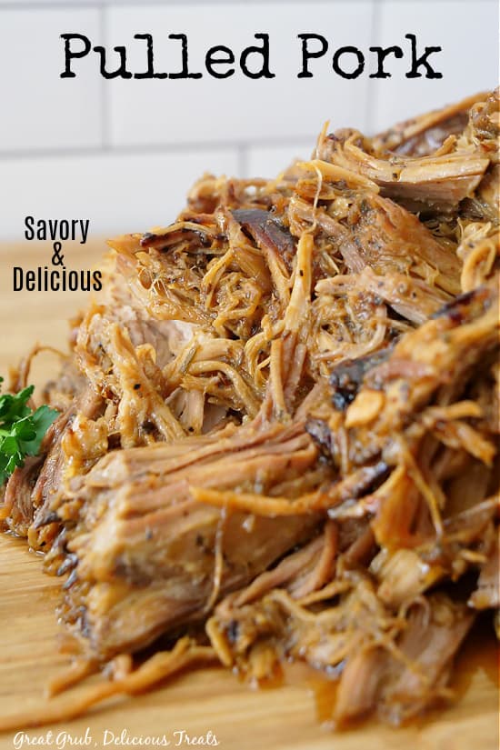 A large wood cutting board piled up with shredded pulled pork.