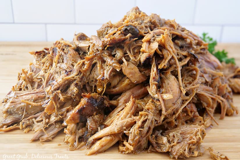 A large pile of pulled pork on a wood cutting board.