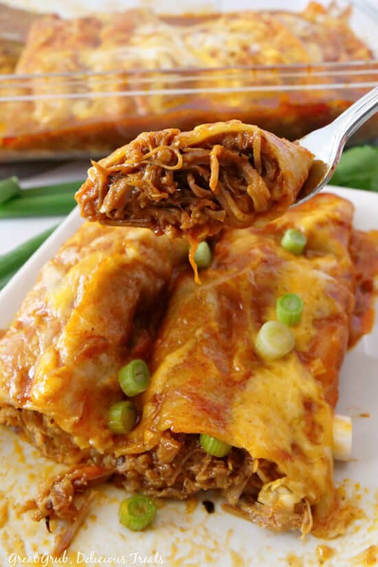 A close up of a bite of enchilada on a fork.