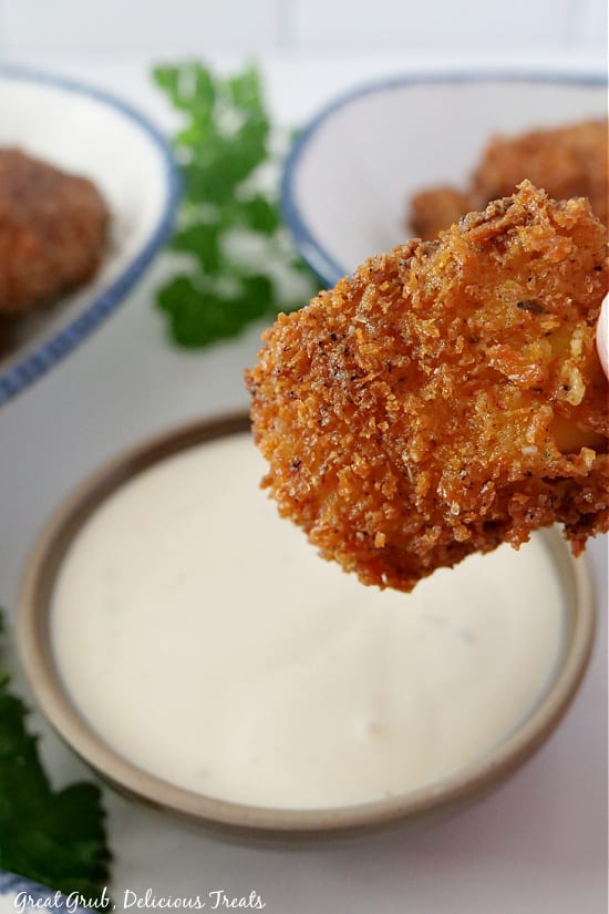 A chicken nugget up close, with a bowl of dipping sauce in the background.