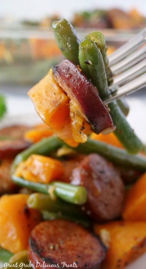 A bite of sweet potato, sausage and green beans on a fork.