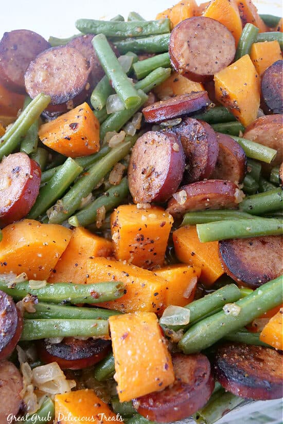 A close up photo of green beans, smoked sausage and sweet potatoes, onions, garlic.